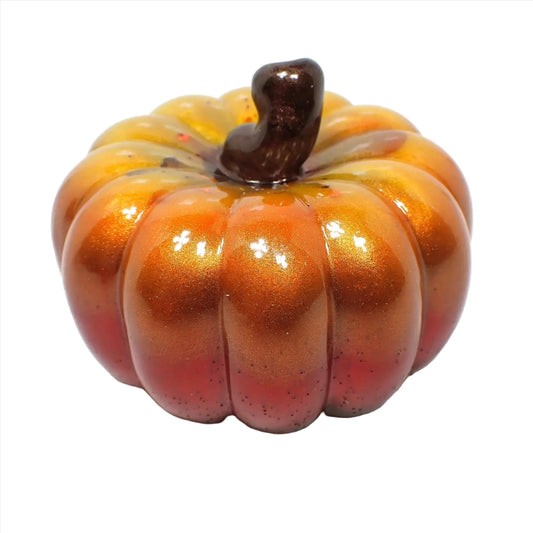 Side view of the small decorative handmade resin pumpkin. It has a pearly brown stem at the top. The rest of the pumpkin has shades of pearly yellow, orange, and red descending down the sides.