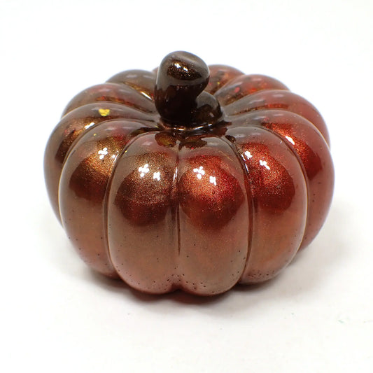 Side view of the handmade small resin decorative pumpkin. It has a pearly brown stem at the top. Most of the pumpkin has shades of pearly brown and red, but there are a few spots of yellow and orange here and there.