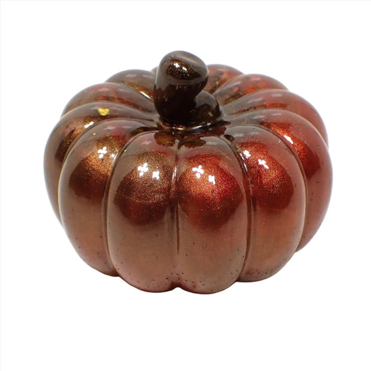 Side view of the handmade small resin decorative pumpkin. It has a pearly brown stem at the top. Most of the pumpkin has shades of pearly brown and red, but there are a few spots of yellow and orange here and there.
