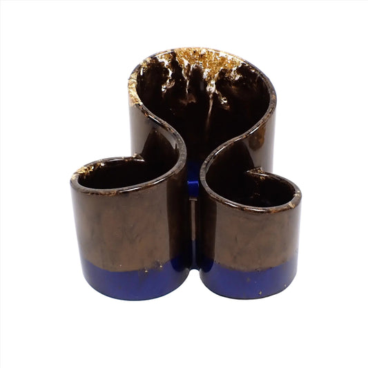 Front view of the handmade makeup brush holder. There are three round areas joined together with the tallest area being in the back. There is pearly dark brown resin on top and dark vivid pearly blue resin at the bottom. There are small areas of metallic gold flake around the top edge areas.