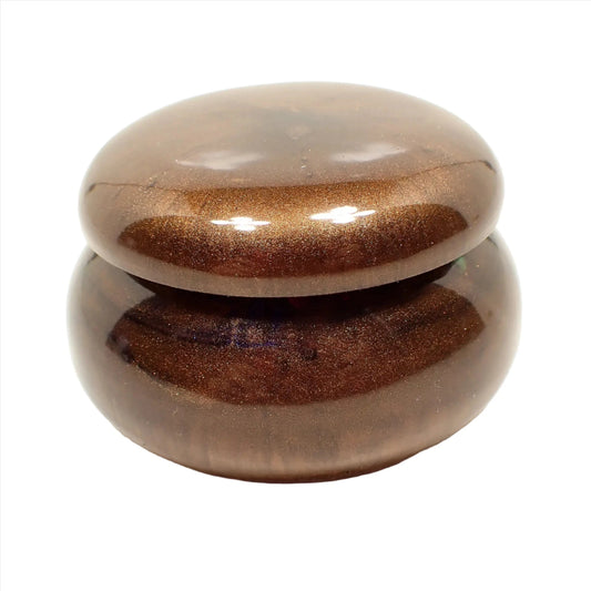 Side view of the handmade resin small trinket box. It has a rounded short jar like shape. It's mostly pearly brown in color with hints of purple seen.