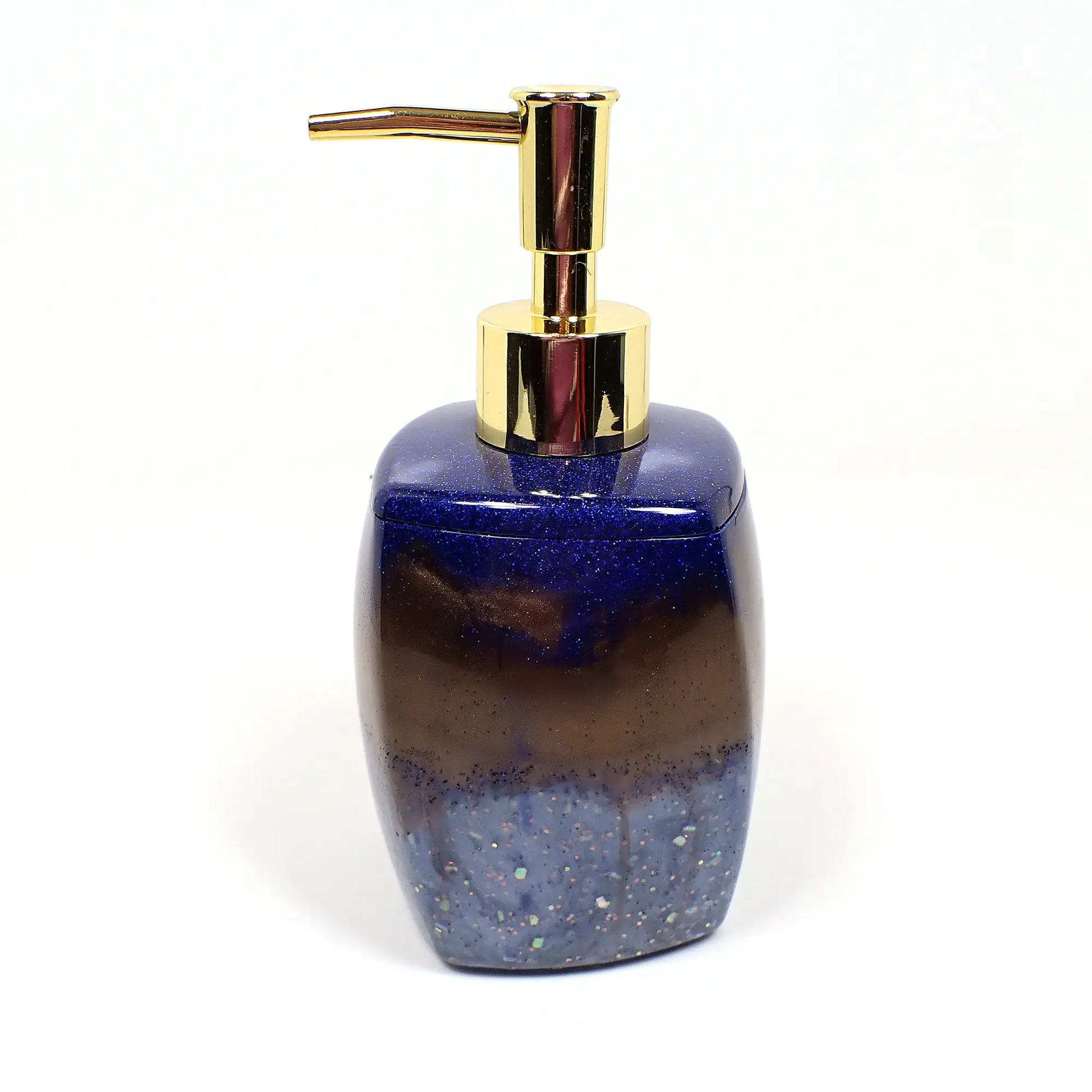 Side view of the handmade resin and glitter soap dispenser. It has a large rounded square design with a light twist to it. There is a gold tone metallic plastic pump style top. The top has pearly dark blue resin with tiny flecks of sparkling blue glitter, the middle area has swirls of pearly dark brown resin, and the bottom has pearly light blue resin with chunky iridescent glitter.