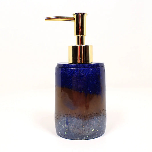 Side view of the handmade resin soap dispenser. In the photo it has a gold tone color pump at the top. The body of the soap dispenser has pearly dark blue resin, then brown, then light blue at the bottom. There is tiny blue glitter at the top and chunky iridescent glitter at the bottom.