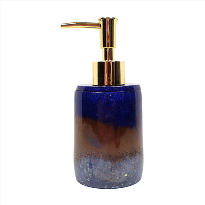 Side view of the handmade resin soap dispenser. In the photo it has a gold tone color pump at the top. The body of the soap dispenser has pearly dark blue resin, then brown, then light blue at the bottom. There is tiny blue glitter at the top and chunky iridescent glitter at the bottom.