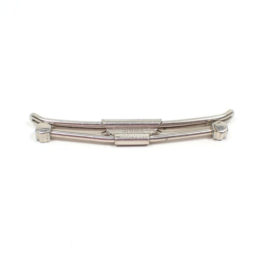 Angled view of the Mid Century vintage Swank 50 collar clip. It is silver tone in color and has a carved bar design with rounded shapes on the ends. 