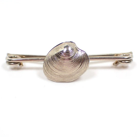 Front view of the retro vintage collar clip. The metal is silver tone in color and the bar has coil ends. There is a seashell shape in the middle of the bar.