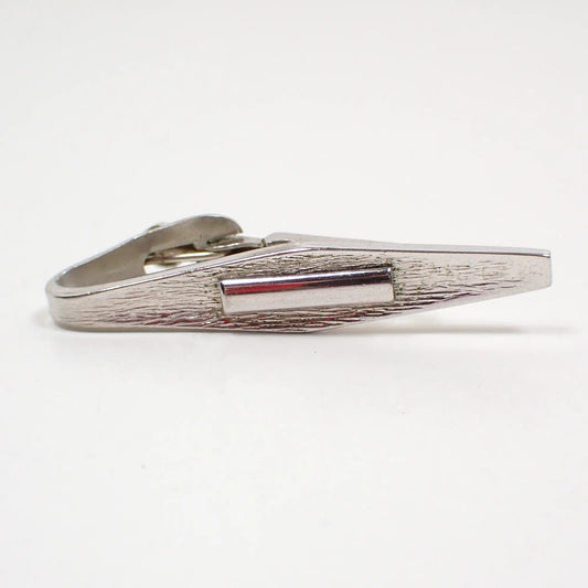 Front view of the mid century vintage Atomic Modernist style tie clip. The metal is silver tone in color. It has an angled marquis shape. The front is textured matte with a small shiny rectangle in the middle.