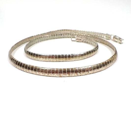 Enlarged side view of the retro vintage omega chain necklace. The metal is silver tone in color, but it has darkened gray areas from age. The are curved long rectangle omega links and a snap lock clasp at the end.
