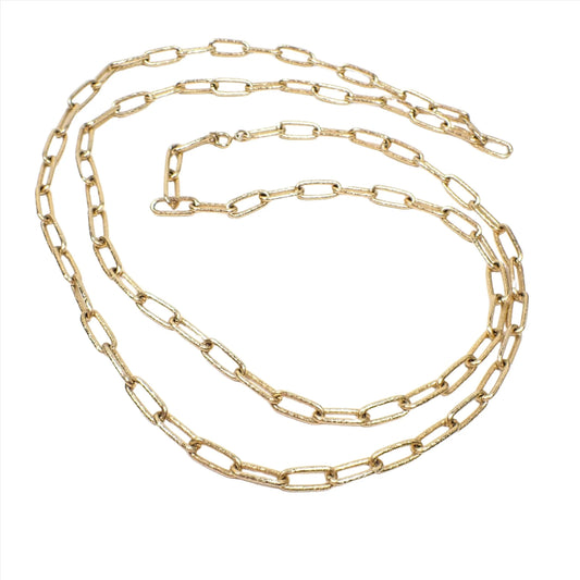 Top view of the retro vintage long maximalist chain necklace. The metal is matte gold tone in color. The long oval cable chain links have a lightly textured pattern on them. There is a spring ring clasp at the end.