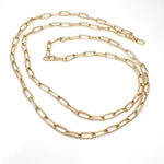 Top view of the retro vintage long maximalist chain necklace. The metal is matte gold tone in color. The long oval cable chain links have a lightly textured pattern on them. There is a spring ring clasp at the end.