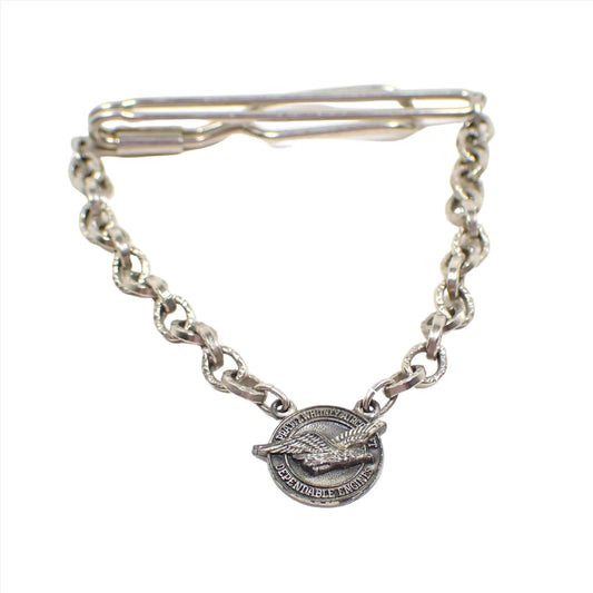 Front view of the Mid Century vintage tie chain bar. The metal is silver tone in color. There is textured cable chain that goes down to a round disk charm at the bottom with an eagle and the words Pratt and Whitney Aircraft Dependable Engines.