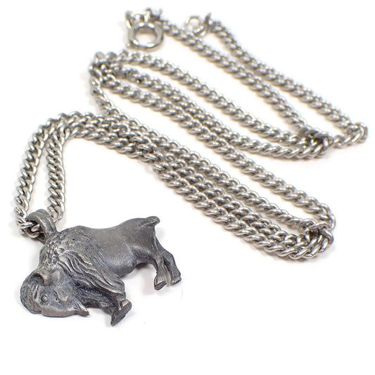 Enlarged top view of the retro vintage Avon pendant necklace. The curb chain is silver tone in color with a spring ring clasp at the end. There is a pewter bison pendant at the bottom of the chain with a built in loop bail. It is dark gray in color.