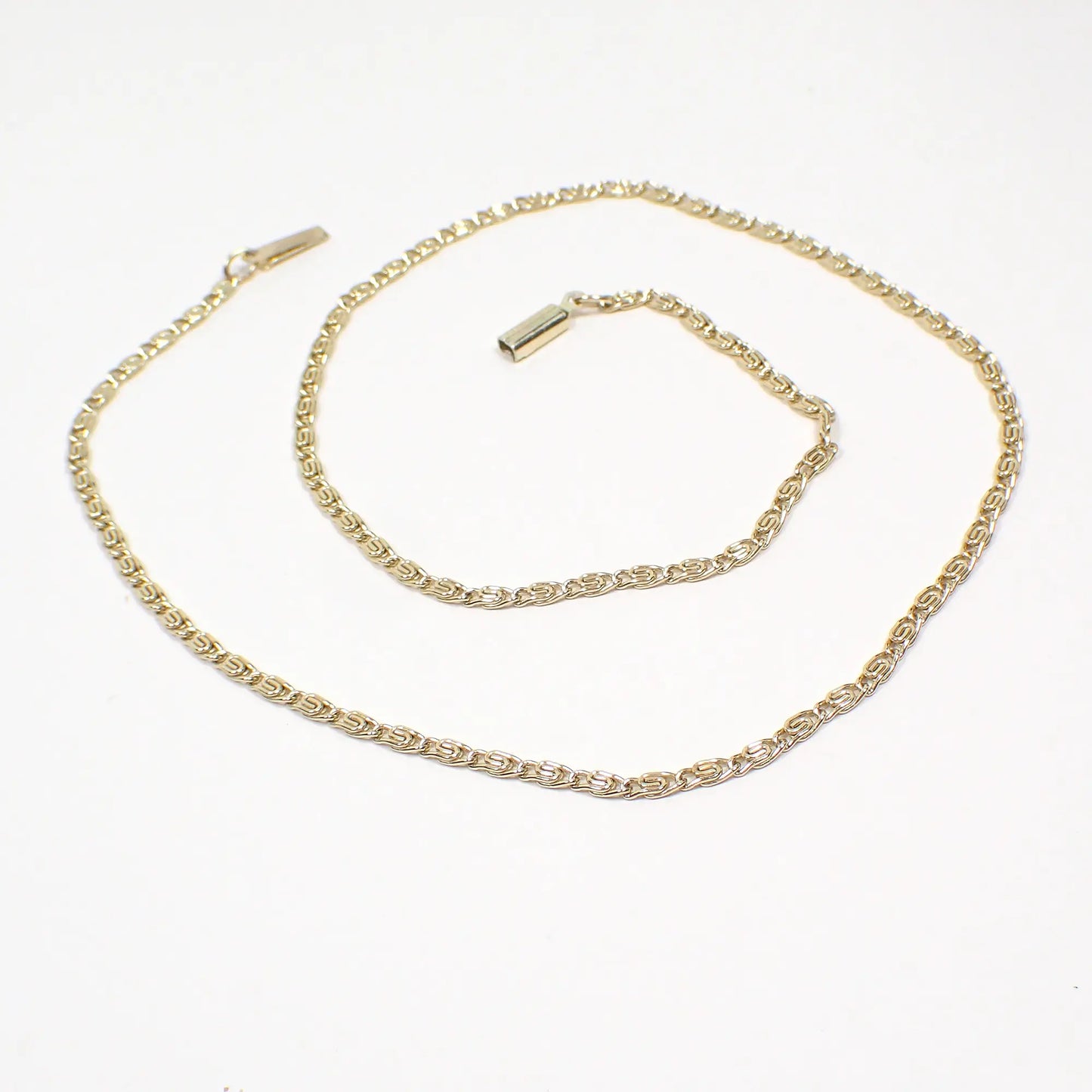 Top view of the Mid Century vintage chain necklace made in Germany. The metal is gold tone in color. The links are small S shaped snail link chain. There is a box clasp and tab at the ends of the chain.