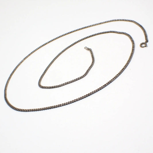 Angled view of the retro vintage Caco sterling silver curb chain necklace. The silver is darkened some from age to a light grey color. The links are smaller sized forming a curb chain. There is a spring ring clasp at one end and a clasp tab at the other with the maker's mark and Sterling on it.