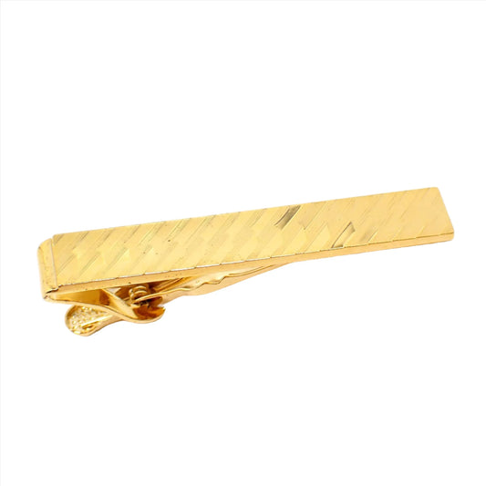Angled view of the retro vintage diamond cut etched tie clip clasp. The metal is gold tone in color. There is an engraved diagonal design on the front.