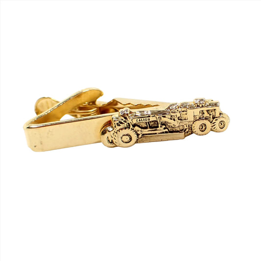 Front view of the Mid Century vintage Mercury Industries tie clip clasp. The metal is gold tone in color. It has a detailed design of a heavy equipment road grader on the end with the name Galion on the front.