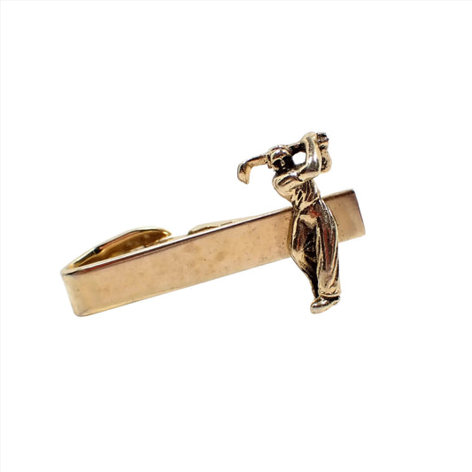 Front view of the Shields Mid Century vintage tie clip clap. The metal is gold tone in color. There is a man swinging a golf club on the end of the tie clip. 