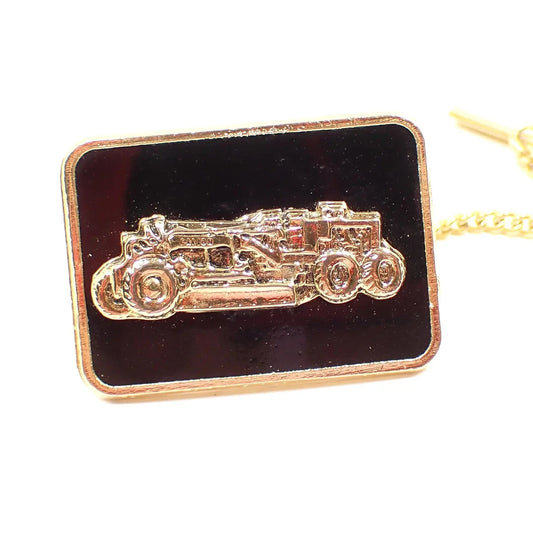 Enlarged front view of the Galion Mid Century vintage advertising tie tack. It is rectangle shaped with rounded corners. The metal is gold tone in color and the background is black enameled. There is a heavy equipment road grader design in the middle.