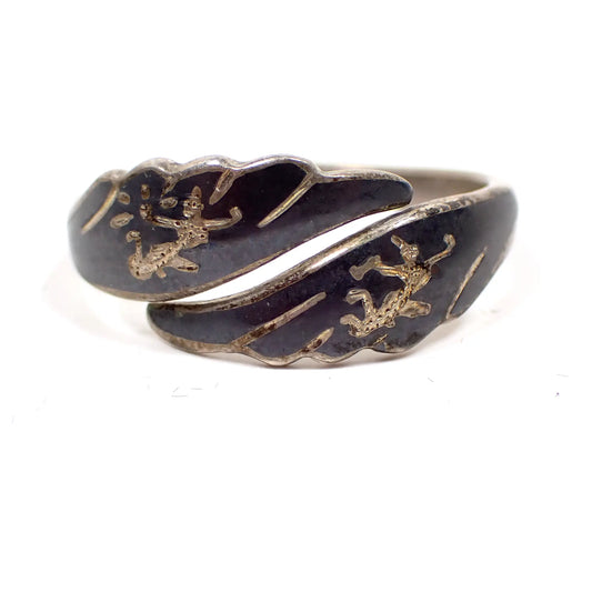 Front view of the Mid Century vintage Siam sterling ring. It has a bypass design with wing like shaped ends.  There is black enamel on the front with etched Siam dancers. 