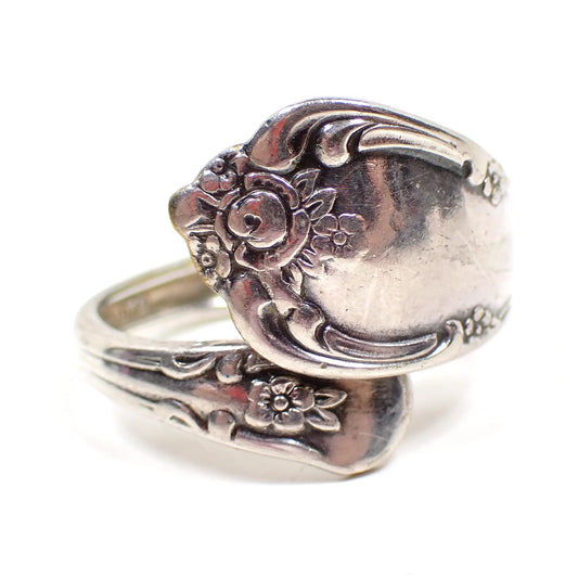 Front view of the WM A Rogers Oneida Ltd spoon ring. It has a bypass design with a flared larger end with a floral pattern and a smaller rounded end with another small flower. The metal is silver tone in color.