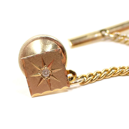 Front view of the Mid Century vintage Emmons 14k gold tie tack. It's shaped like a square with an engraved atomic starburst design. There is a tiny diamond chip accent in the center.