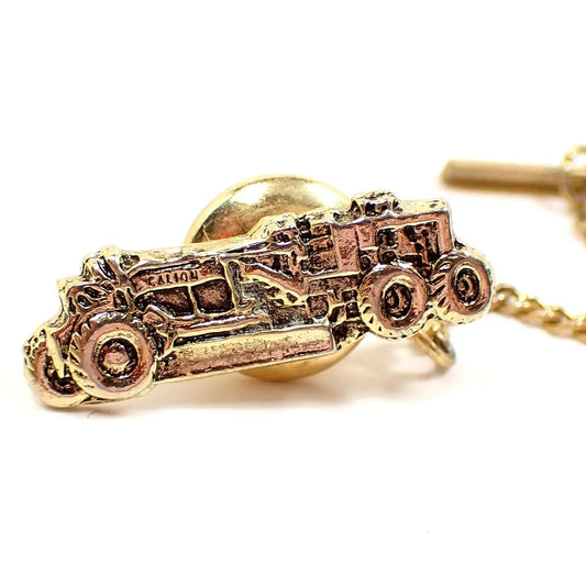 Enlarged front view of the Mid Century vintage Galion tie tack. The metal is gold tone in color. It is shaped like a road grader heavy equipment. 