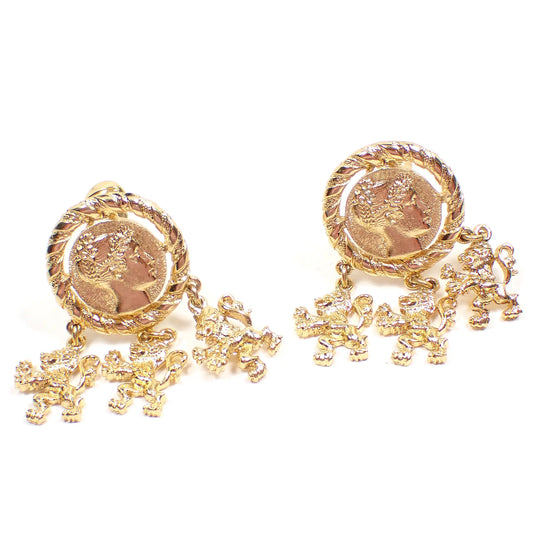 Front view of the retro vintage Monet clip on earrings. The metal is gold tone in color. The tops are round with Roman head design. There are three roaring lion dangles at the bottom of each earring.