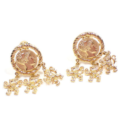 Front view of the retro vintage Monet clip on earrings. The metal is gold tone in color. The tops are round with Roman head design. There are three roaring lion dangles at the bottom of each earring.