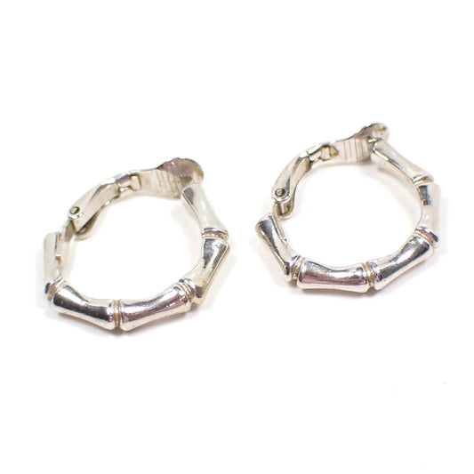 Side view of the retro vintage Crown Trifari hoop earrings. The metal is silver tone in color. They have a bamboo shaped rounded design. The clips on backs can be seen in the photo.