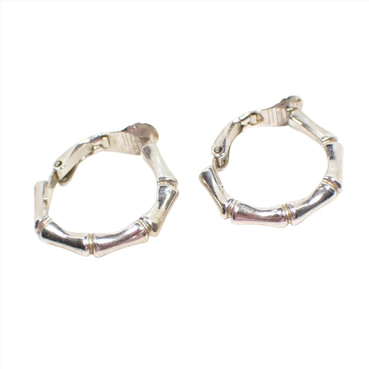 Side view of the retro vintage Crown Trifari hoop earrings. The metal is silver tone in color. They have a bamboo shaped rounded design. The clips on backs can be seen in the photo.