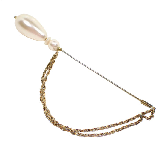Side view of the retro vintage beaded hat pin. There is a plastic off white teardrop shaped faux pearl at the top and a saucer and round plastic faux pearl bead below it. The metal is gold tone in color. There are two strands of small rope chain going from the bottom of the beads down to the pin clutch.