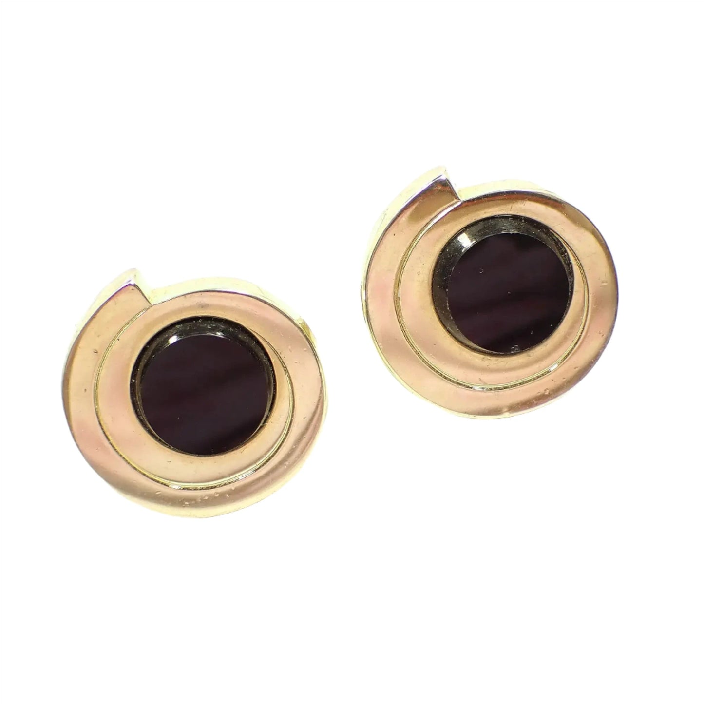 Angled front view of the retro vintage Pierre Cardin cufflinks. The metal is gold tone in color. They look like a bar that is shaped around itself in a circle shape. There are round flat top black onyx gemstone cabs in the middle.