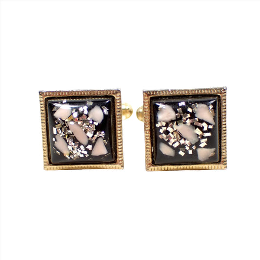 Front view of the Anson Mid Century vintage cufflinks. The metal is gold tone in color. The cuff links are square with domed confetti lucite cabs that have bits of light pink, gold, and silver color on a black background.