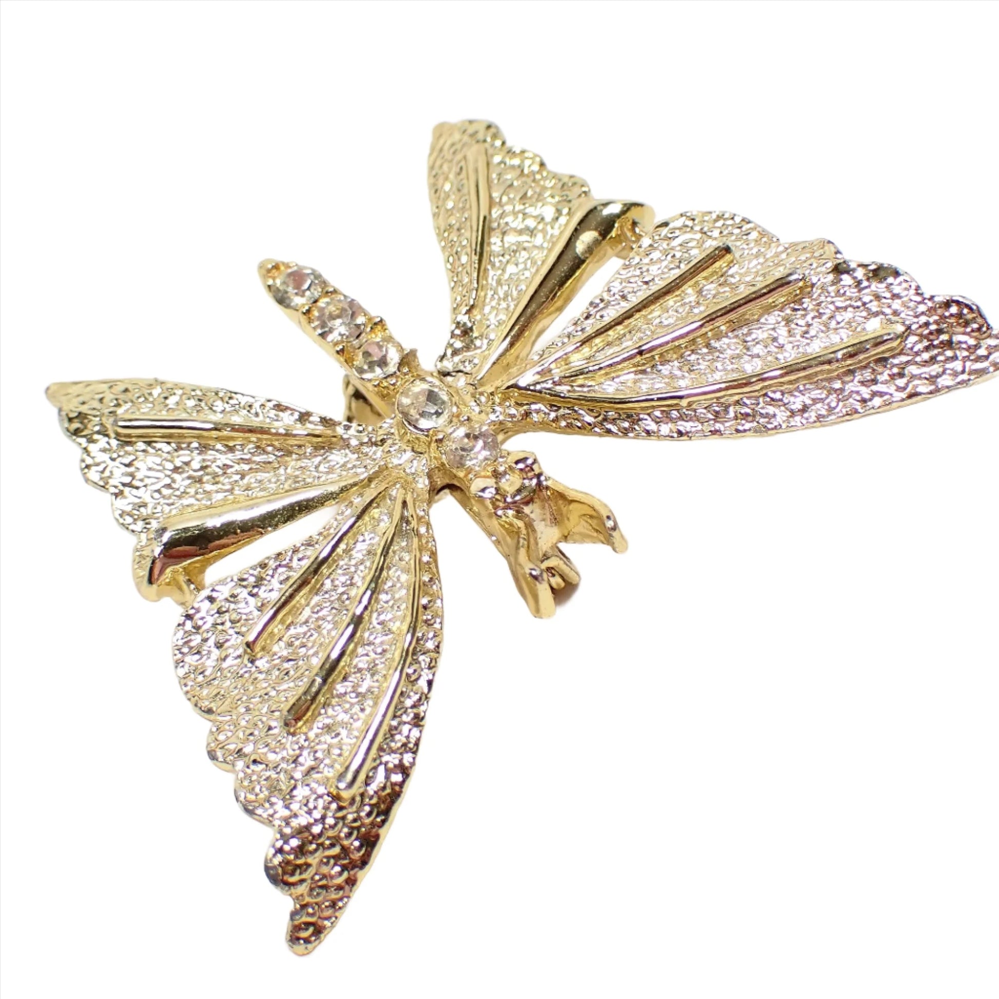 Angled view of the retro vintage Gerry's brooch pin. It's shaped like a butterfly with clear rhinestones down the body of the butterfly. The metal is gold tone in color and the wings have a bumpy textured pattern.