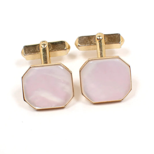 Front view of the Mid Century vintage Swank cufflinks. The metal is gold tone in color. The fronts are shaped like wide octagons. There are pearly white mother of pearl shell cabs on the front. 