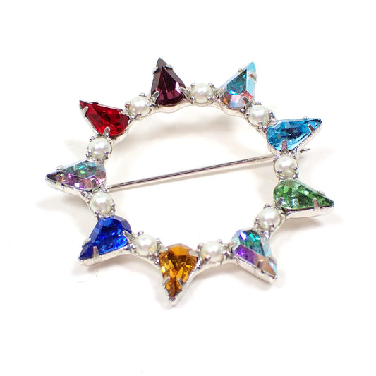 Front view of the Mid Century vintage B David open starburst brooch pin. The metal is silver tone in color. There are teardrop shaped rhinestones in various colors going around the brooch. Some have an iridescent AB coating. In between each rhinestone is a tiny faux pearl.