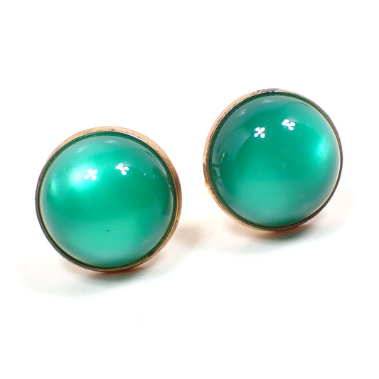 Front view of the Mid Century vintage moonglow lucite cufflinks. They are round with a gold tone color metal setting. The lucite cabs are domed and are green in color. They have an inner glow like appearance where the light is hitting them.