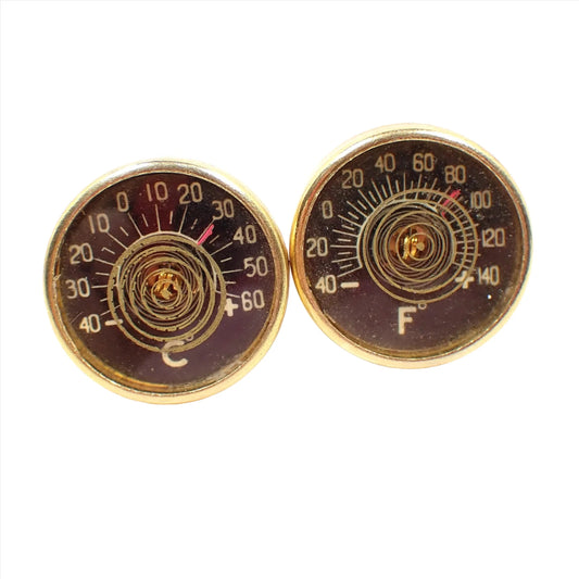 Front view of the Mid Century vintage Harvey Avedon cufflinks. They are round and have thermometers on the inside. One is for Celsius and the other is Fahrenheit. The metal is gold tone in color.
