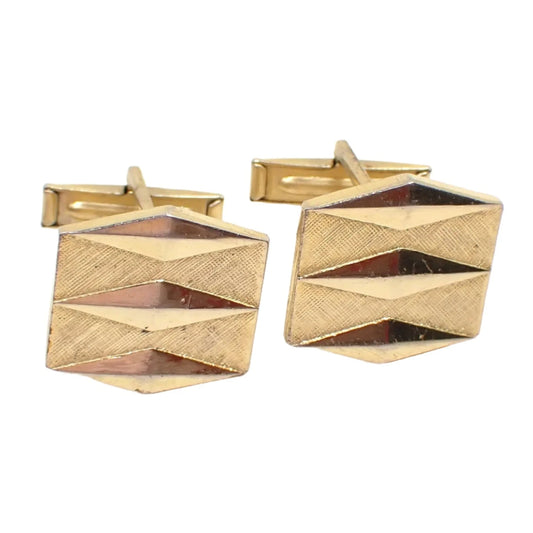 Front view of the Mid Century vintage Atomic style cufflinks. The metal on the cuff links is gold tone in color. They are hexagon shaped with a brushed matte front and three cut elongated diamond shapes on the front.