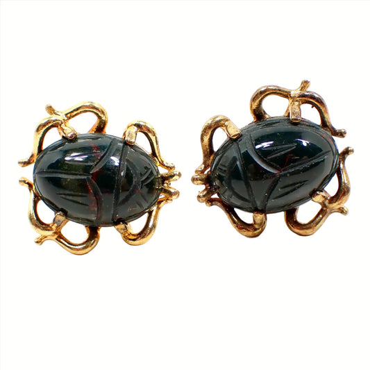 Front view of the Dolan Bullock Mid Century vintage cufflinks. The metal is gold tone in color an is shaped like scarab legs with open areas on the inside. The middle of the cufflinks have oval glass cabs that are carved to look like scarabs and are dark green in color with small bits of orange here and there.
