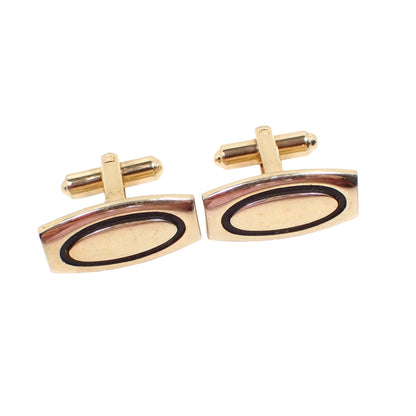 Angled view of the Hickok Mid Century vintage cufflinks. They are gold tone in color. The fronts are slightly curved with a Modernist style rectangle shape with curved top and bottom. There are black ovals in the middle.