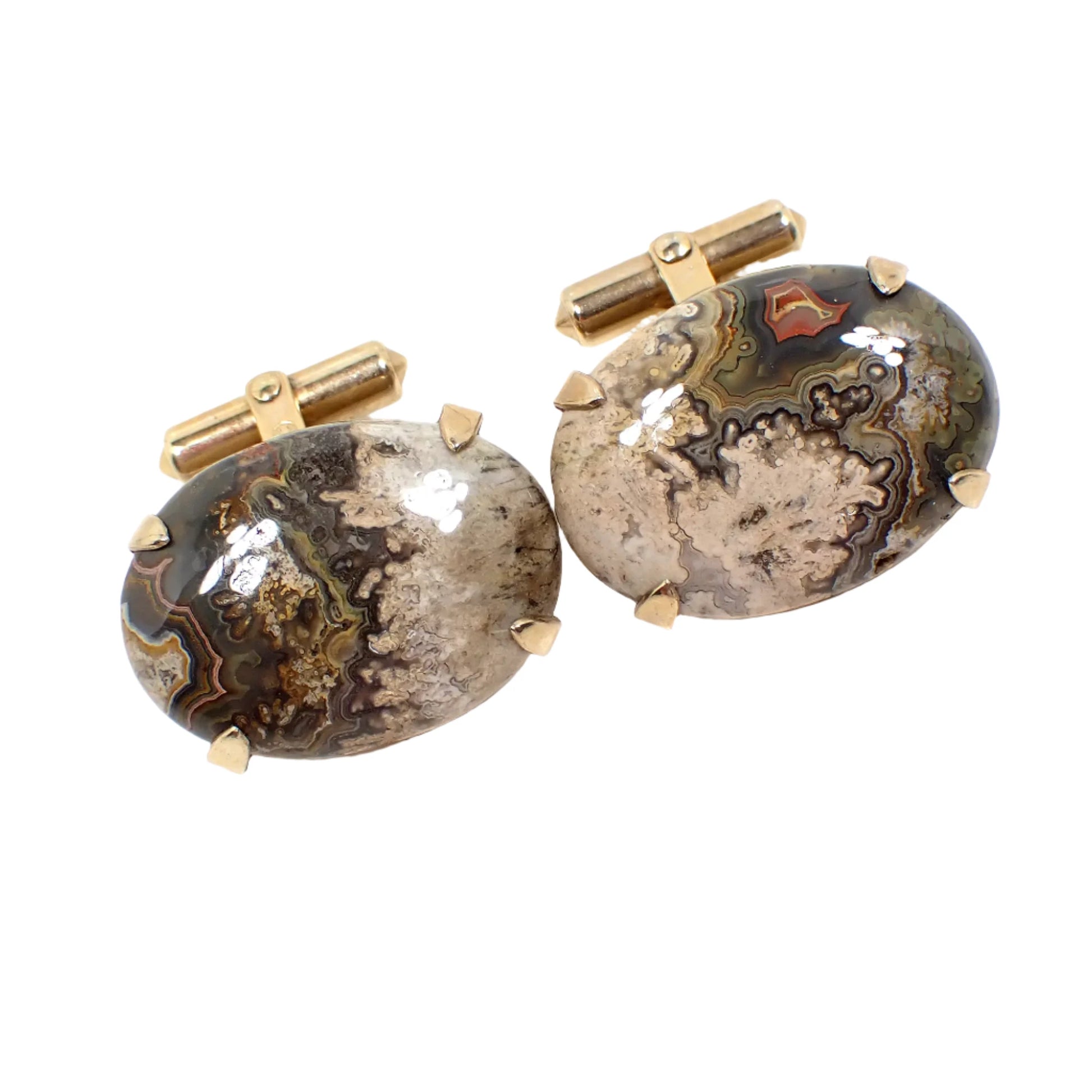 Angled view of the Mid Century vintage Destino gemstone cufflinks. The cuff link settings are gold filled. There are domed oval jasper cabs on the front with marbled shades of cream, brown, green, and red. The cabs are prong set. 