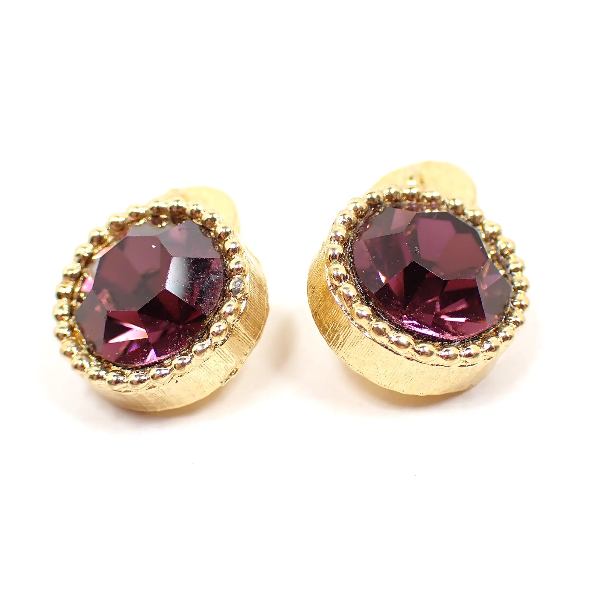 Angled view of the Mid Century vintage rhinestone bridge cufflinks. They are round in shape. The metal is gold tone in color and has a round dot pattern around the front edge. There are dark purple rhinestones in the middle.