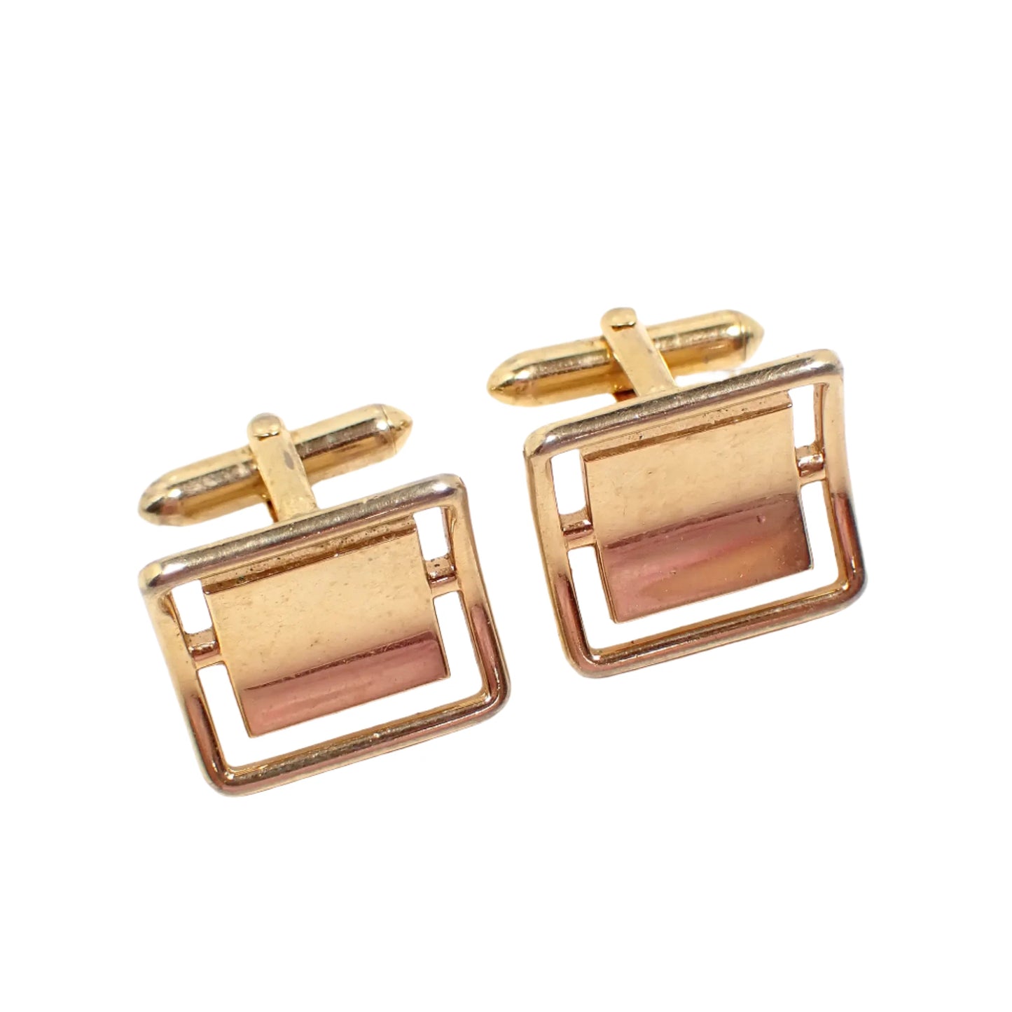 Angled front view of the Mid Century Swank vintage cufflinks. The metal is gold tone in color. They are shaped like squares that are curved and have a cut out area around the edge. 