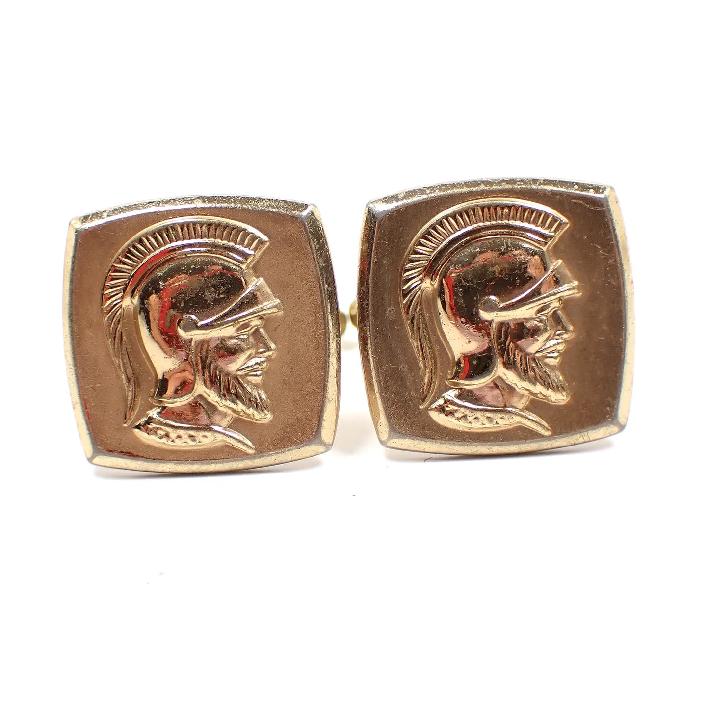 Enlarged front view of the Hickok Mid Century vintage cufflinks. They are curved square shape and gold tone metal in color. There is a raised metal cameo of Roman soldier heads on the front.