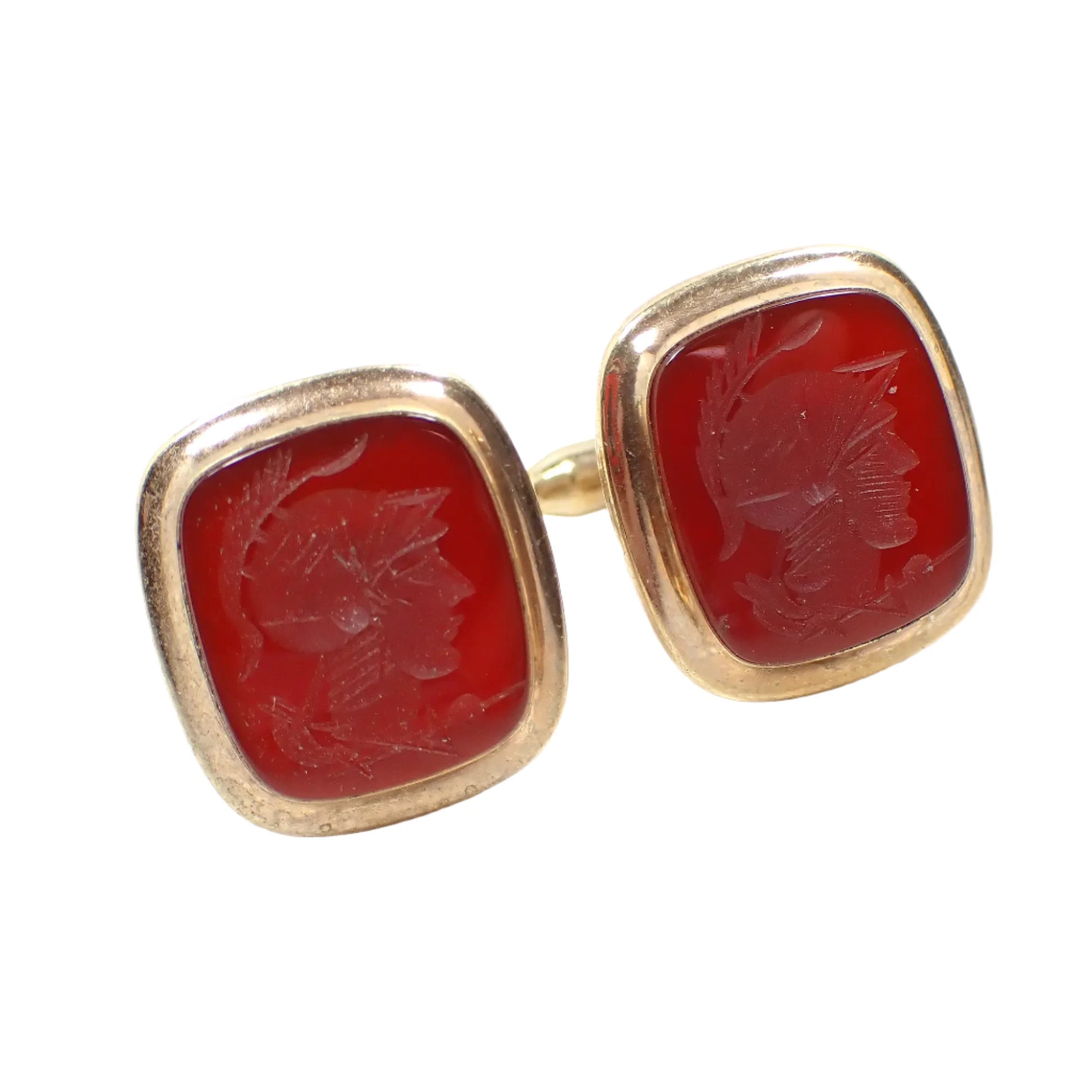 Angled front view of the 1940's Vintage Dolan and Bullock cufflinks. The metal is gold filled and shaped like rounded rectangles. They have dark reddish orange color carnelian cabs on the front. The cabs have a carved intaglio cameo design of a Roman soldier's head.