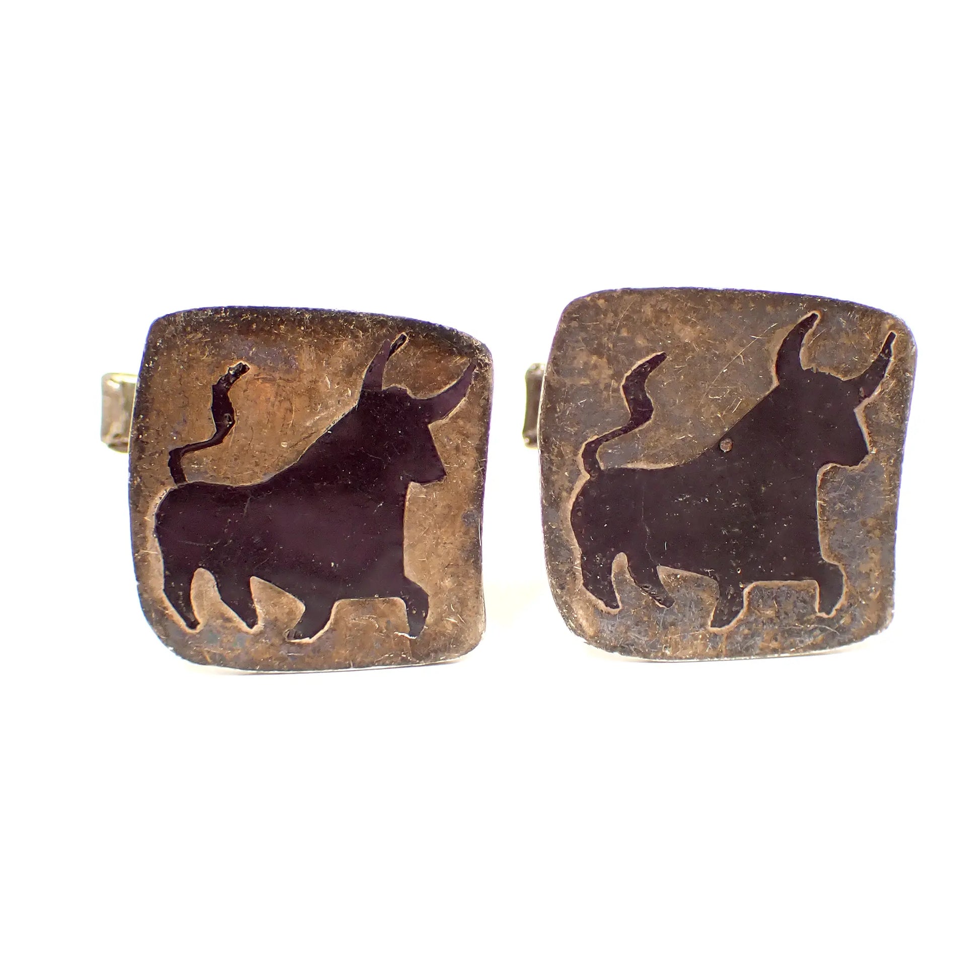 Front view of the retro vintage Taxco cufflinks. They are square in shape with rounded corners. They are a dark gray in color with a black bull design in the middle. 