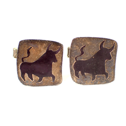 Front view of the retro vintage Taxco cufflinks. They are square in shape with rounded corners. They are a dark gray in color with a black bull design in the middle. 