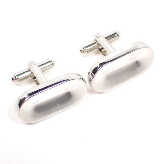 Angled front view of the retro vintage Hickok cufflinks. The metal is silver tone in color. They are shaped like long ovals with an indented middle area