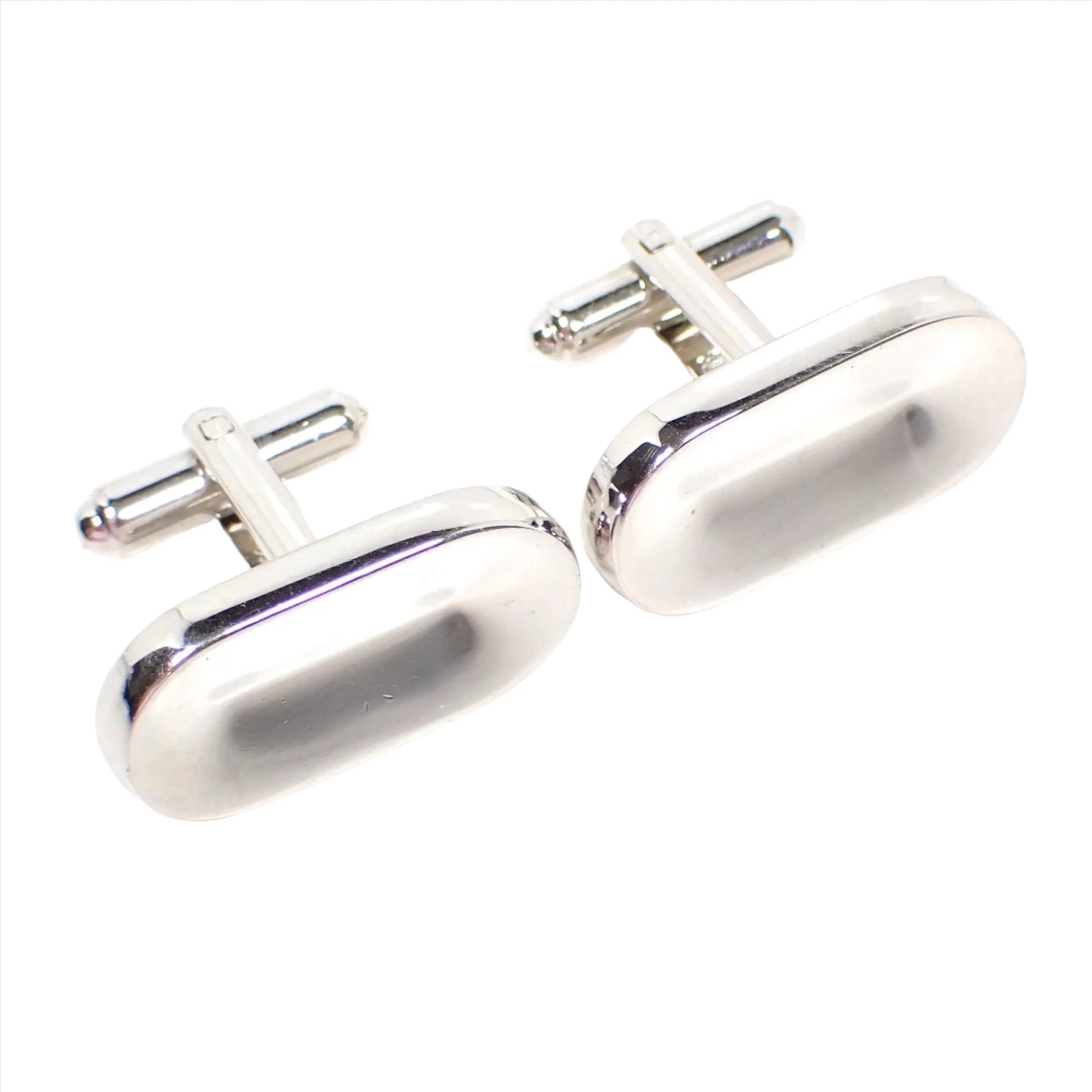 Angled front view of the retro vintage Hickok cufflinks. The metal is silver tone in color. They are shaped like long ovals with an indented middle area